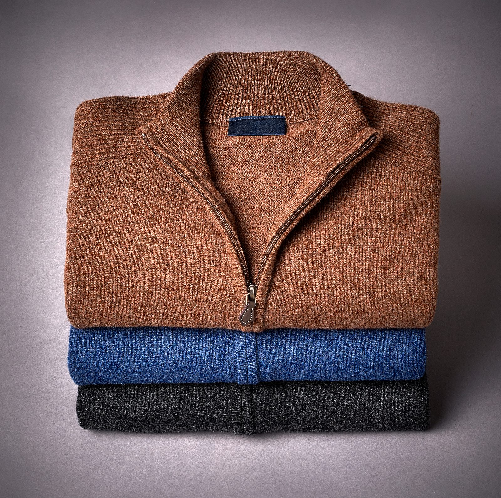 Stack of folded zip-neck sweaters in rust, blue and charcoal